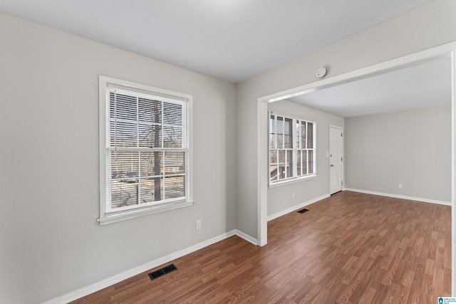 empty room featuring wood finished floors, visible vents, and baseboards