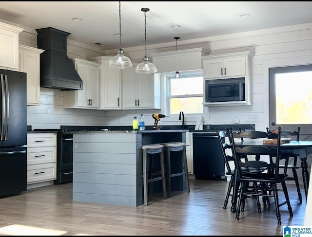 kitchen featuring premium range hood, dark countertops, black appliances, and light wood-style flooring