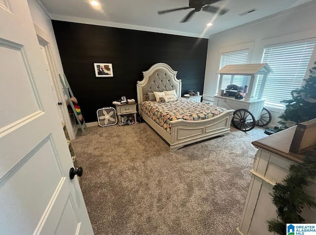 carpeted bedroom featuring visible vents, ornamental molding, a ceiling fan, wood walls, and an accent wall