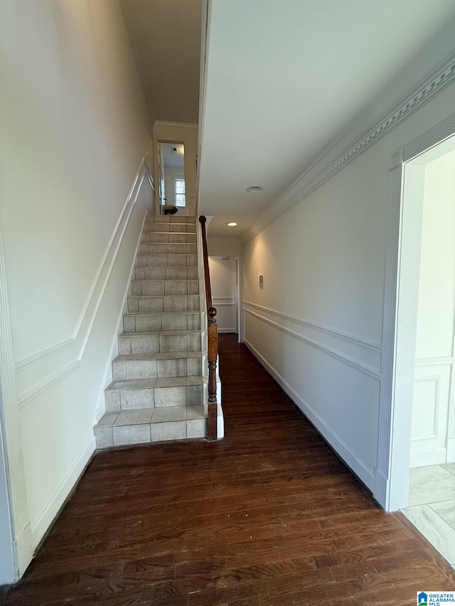 stairs with wainscoting, wood finished floors, ornamental molding, and a decorative wall