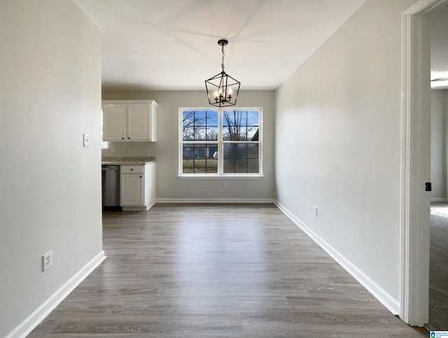 unfurnished dining area with baseboards, an inviting chandelier, and wood finished floors