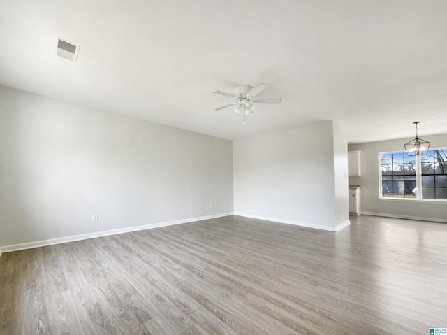 empty room with wood finished floors, ceiling fan with notable chandelier, visible vents, and baseboards