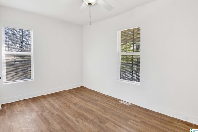 spare room featuring ceiling fan, visible vents, baseboards, and wood finished floors