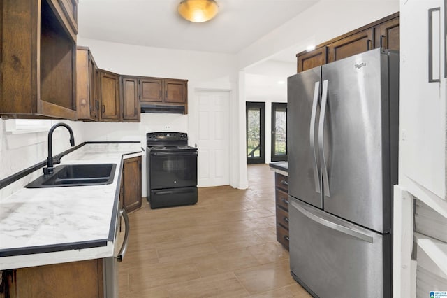 kitchen with a sink, under cabinet range hood, black range with electric cooktop, freestanding refrigerator, and light countertops