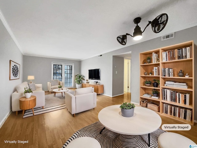 living room with visible vents, baseboards, ornamental molding, and light wood finished floors