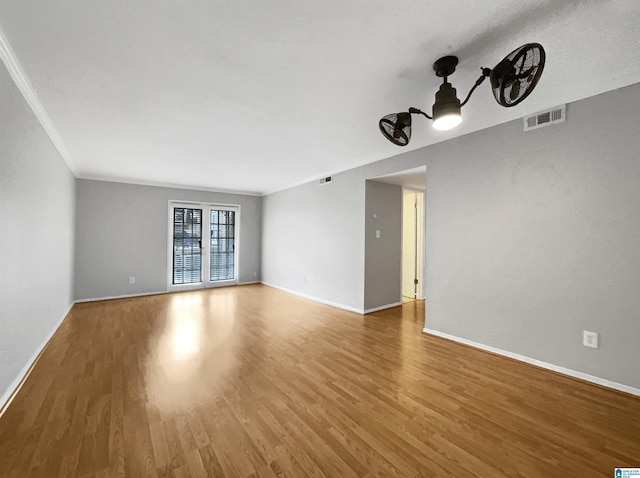 spare room with visible vents, crown molding, baseboards, and wood finished floors