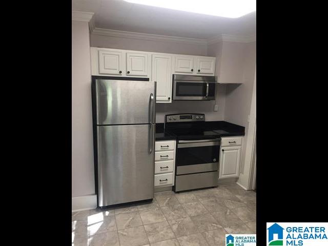 kitchen with dark countertops, appliances with stainless steel finishes, ornamental molding, and white cabinets