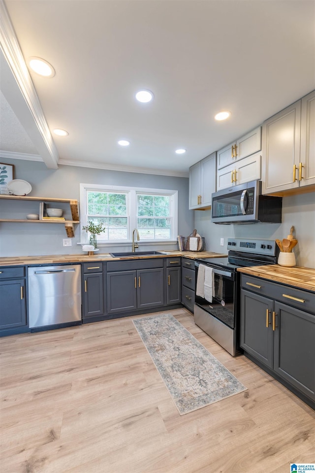 kitchen with light wood finished floors, stainless steel appliances, crown molding, and a sink