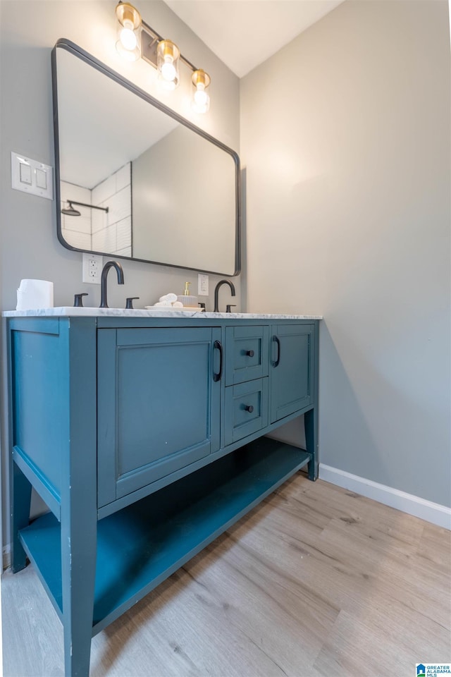 full bath with double vanity, a sink, baseboards, and wood finished floors