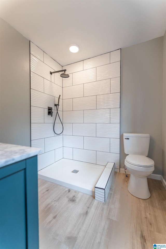 bathroom featuring baseboards, toilet, wood finished floors, and a tile shower