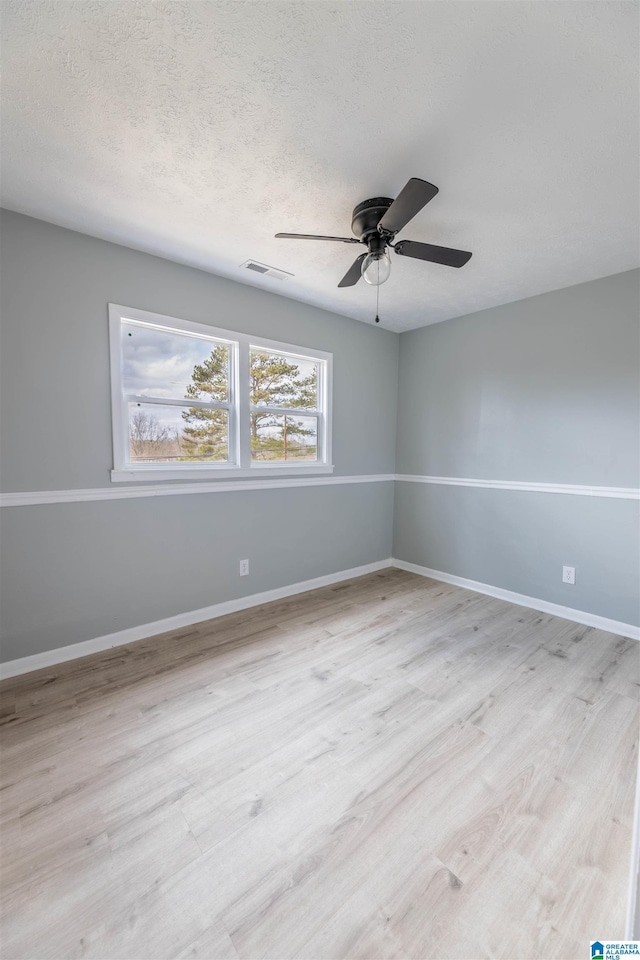 unfurnished room featuring visible vents, light wood-style flooring, a ceiling fan, a textured ceiling, and baseboards