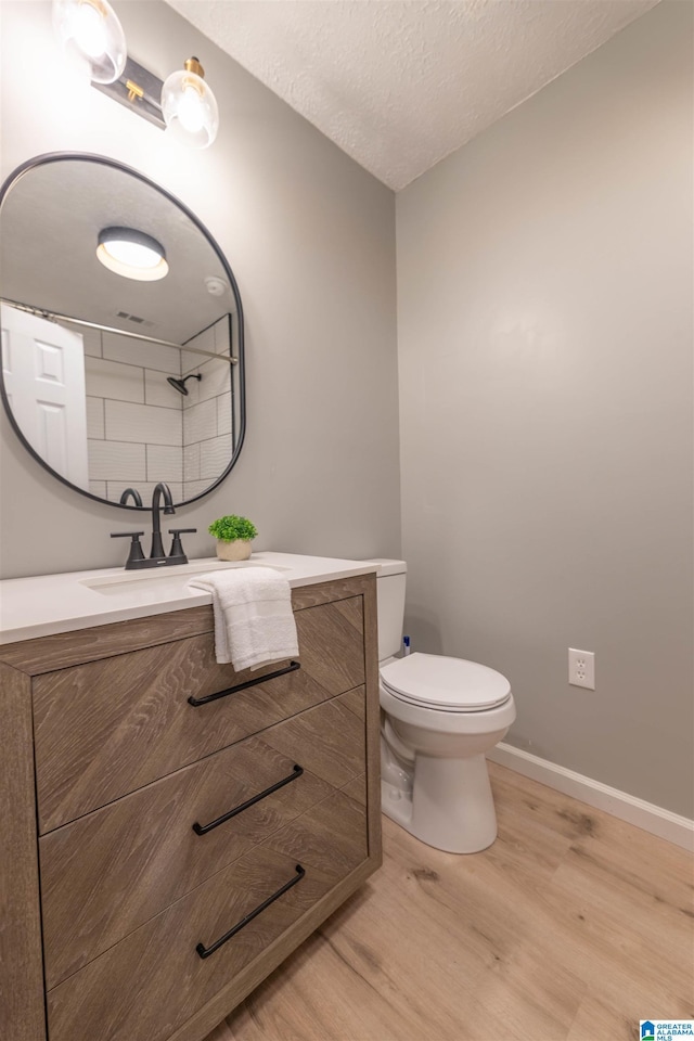 bathroom with baseboards, toilet, vanity, wood finished floors, and a textured ceiling