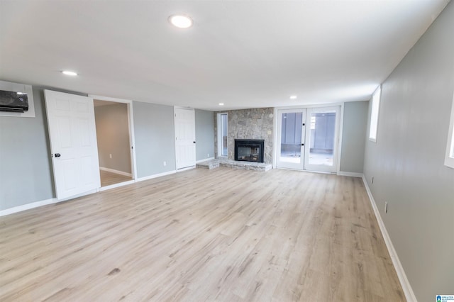 unfurnished living room with a wall unit AC, recessed lighting, a stone fireplace, light wood finished floors, and baseboards