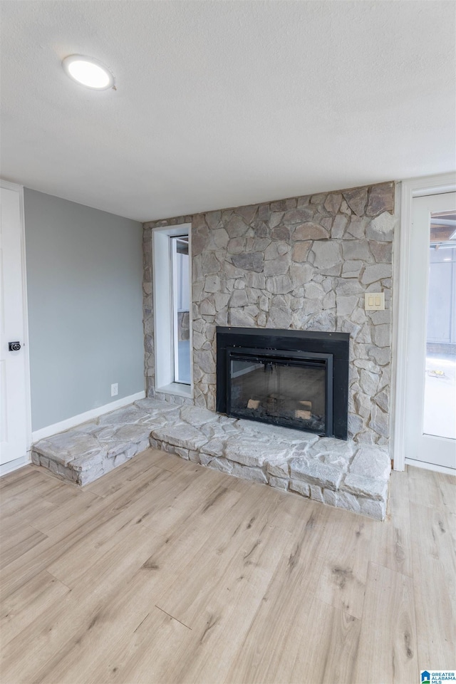 unfurnished living room with wood finished floors, a fireplace, baseboards, and a textured ceiling