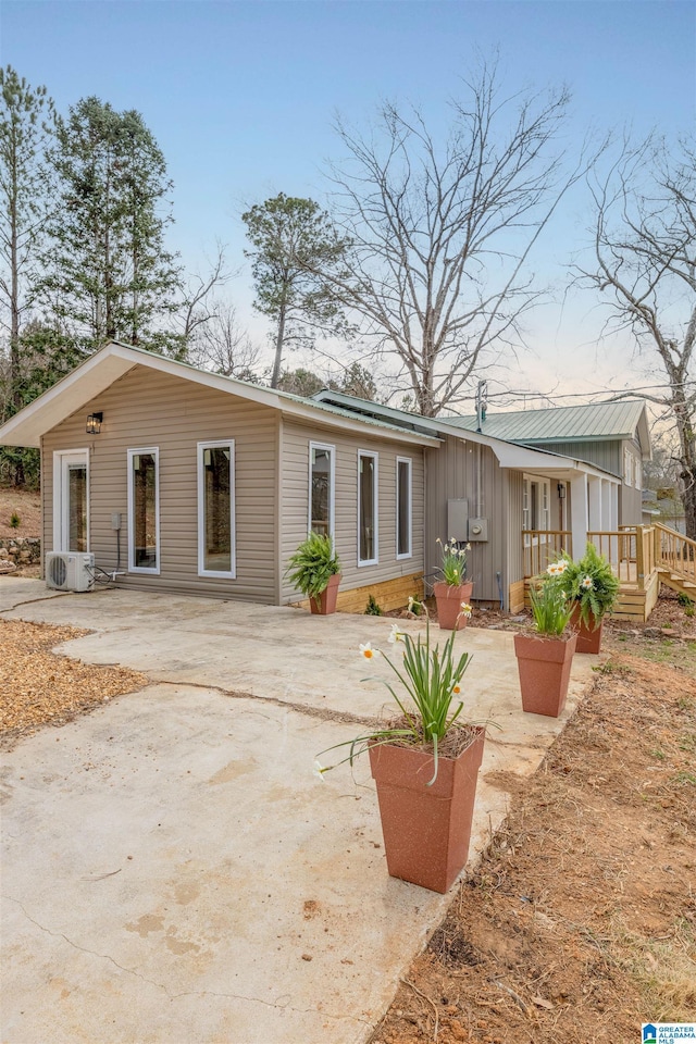 back of property with ac unit, roof mounted solar panels, board and batten siding, and a patio