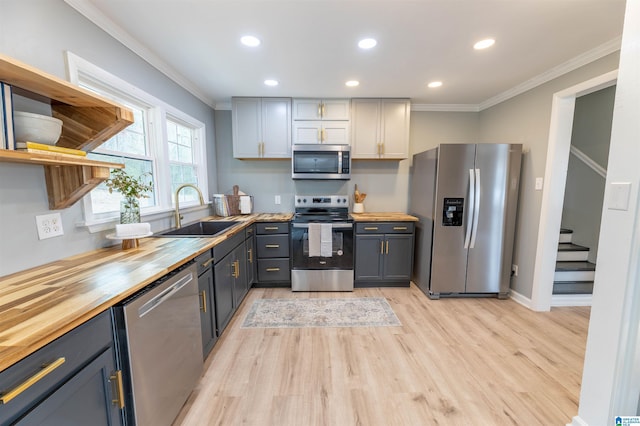 kitchen with a sink, butcher block counters, ornamental molding, stainless steel appliances, and open shelves