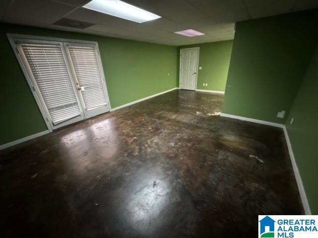 spare room with unfinished concrete flooring, a paneled ceiling, and baseboards