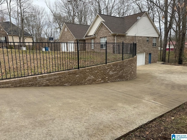 view of side of property with brick siding, concrete driveway, a garage, and fence