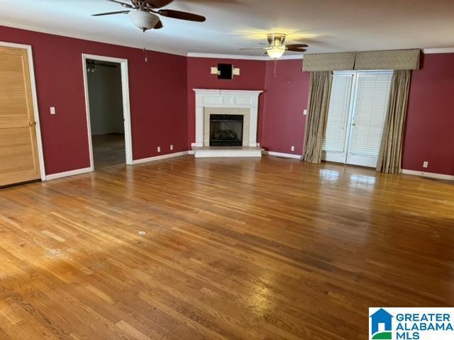 unfurnished living room with baseboards, wood finished floors, a fireplace, and a ceiling fan