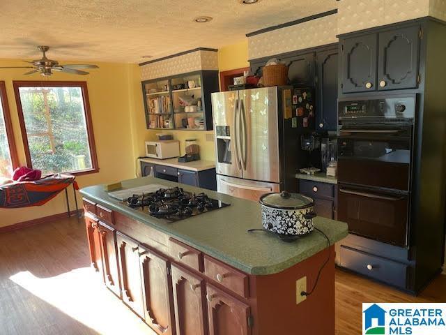 kitchen featuring wood finished floors, baseboards, black appliances, a textured ceiling, and a center island