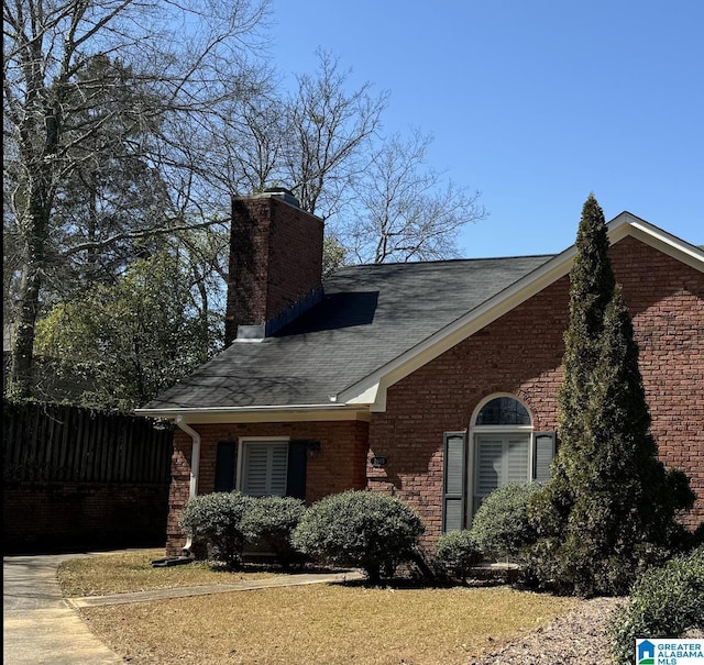 view of home's exterior with fence, a shingled roof, a chimney, a lawn, and brick siding