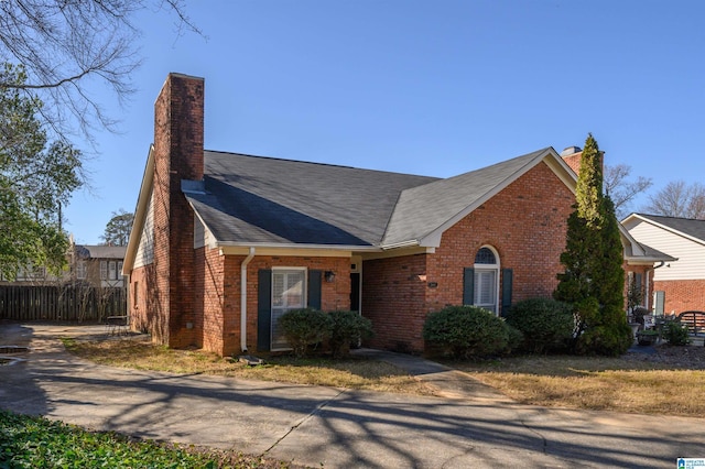 view of front of home with brick siding, a chimney, roof with shingles, and fence