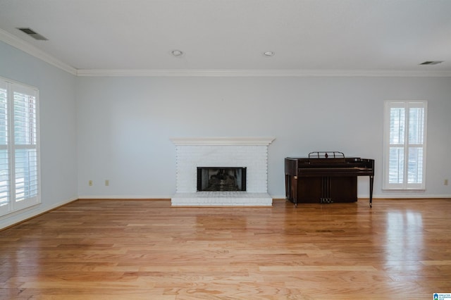 unfurnished living room featuring light wood-type flooring, visible vents, ornamental molding, baseboards, and a brick fireplace