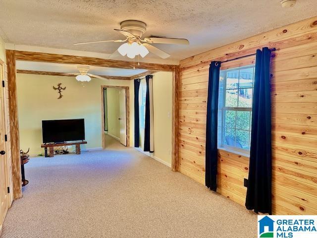 unfurnished living room featuring light carpet, a textured ceiling, ceiling fan, and wooden walls