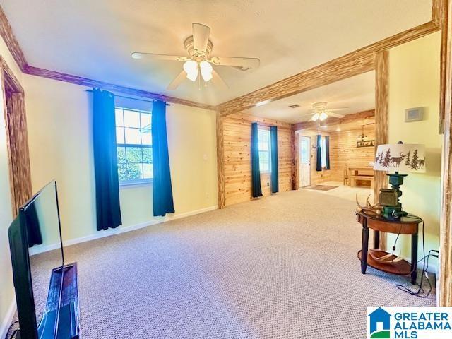 interior space with ceiling fan, baseboards, wood walls, and crown molding