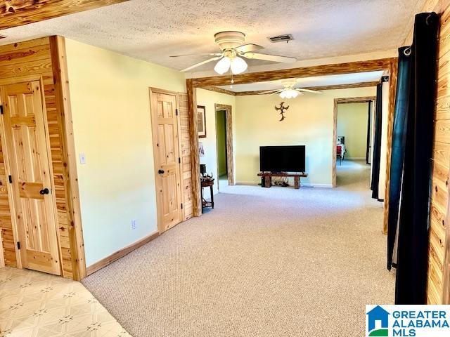 interior space featuring baseboards, visible vents, ceiling fan, a textured ceiling, and light colored carpet