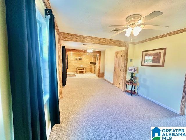 hall featuring visible vents, wood walls, carpet flooring, crown molding, and baseboards