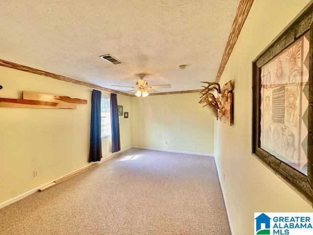 empty room with carpet, visible vents, ceiling fan, a textured ceiling, and crown molding