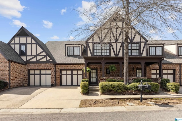 tudor home with brick siding, covered porch, an attached garage, and a shingled roof