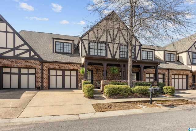 english style home with brick siding, covered porch, driveway, and roof with shingles