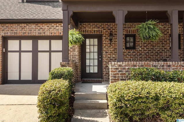 property entrance featuring an attached garage, brick siding, driveway, and roof with shingles