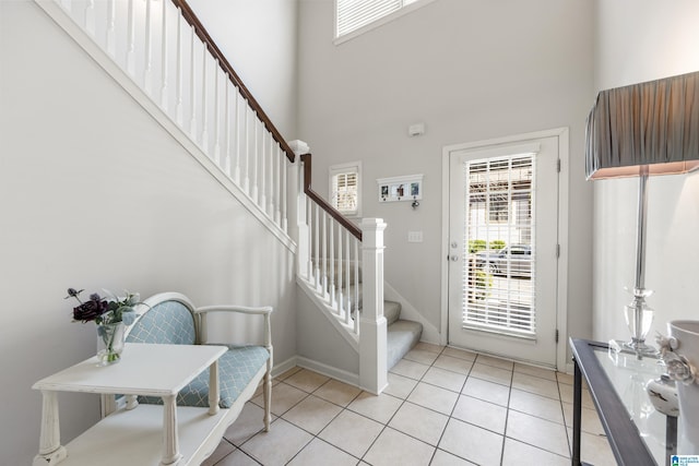 entryway with a wealth of natural light, light tile patterned floors, stairway, and a towering ceiling