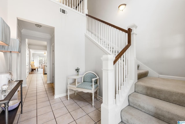 stairway with visible vents, a high ceiling, crown molding, tile patterned flooring, and baseboards