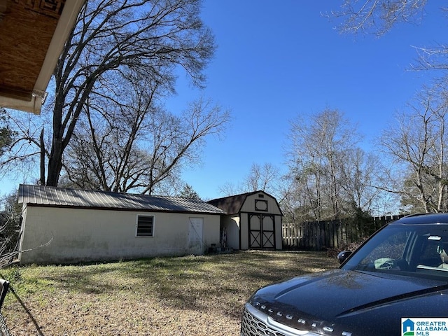 view of property exterior with metal roof, a barn, an outdoor structure, and fence