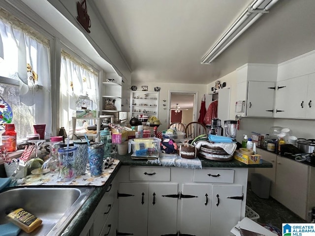 kitchen featuring a peninsula, white cabinets, dark countertops, and a sink