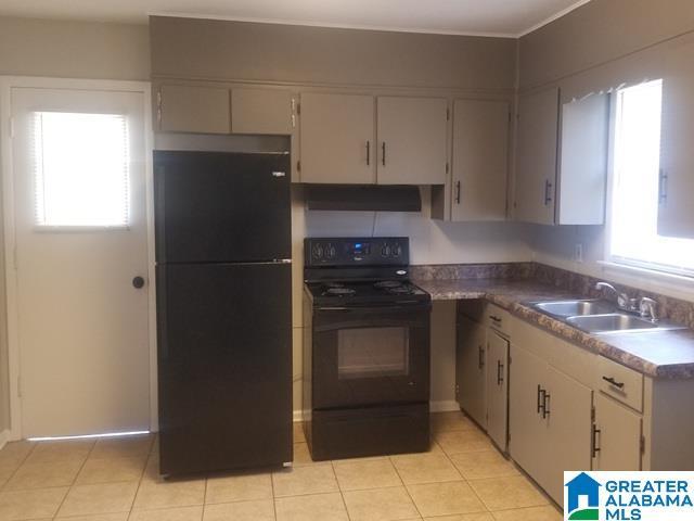 kitchen with under cabinet range hood, light tile patterned floors, black appliances, and a sink