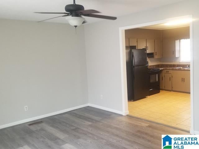 kitchen featuring baseboards, ceiling fan, black appliances, dark countertops, and light wood-type flooring