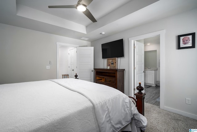 carpeted bedroom featuring ensuite bath, baseboards, a tray ceiling, and a ceiling fan