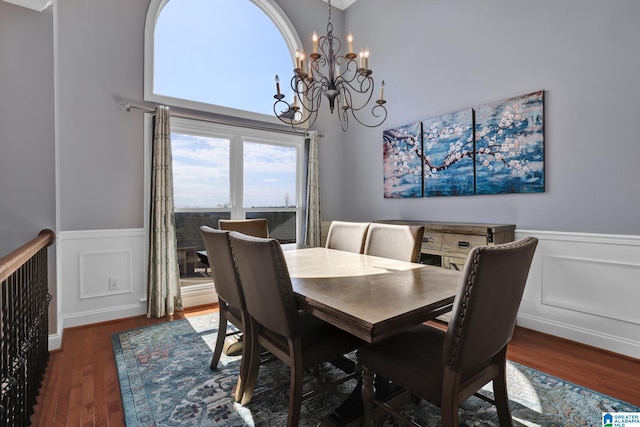 dining space with an inviting chandelier, a decorative wall, wood finished floors, and a wainscoted wall