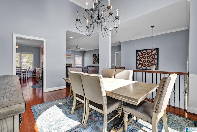 dining area with wood finished floors, baseboards, a fireplace, ornamental molding, and ceiling fan with notable chandelier