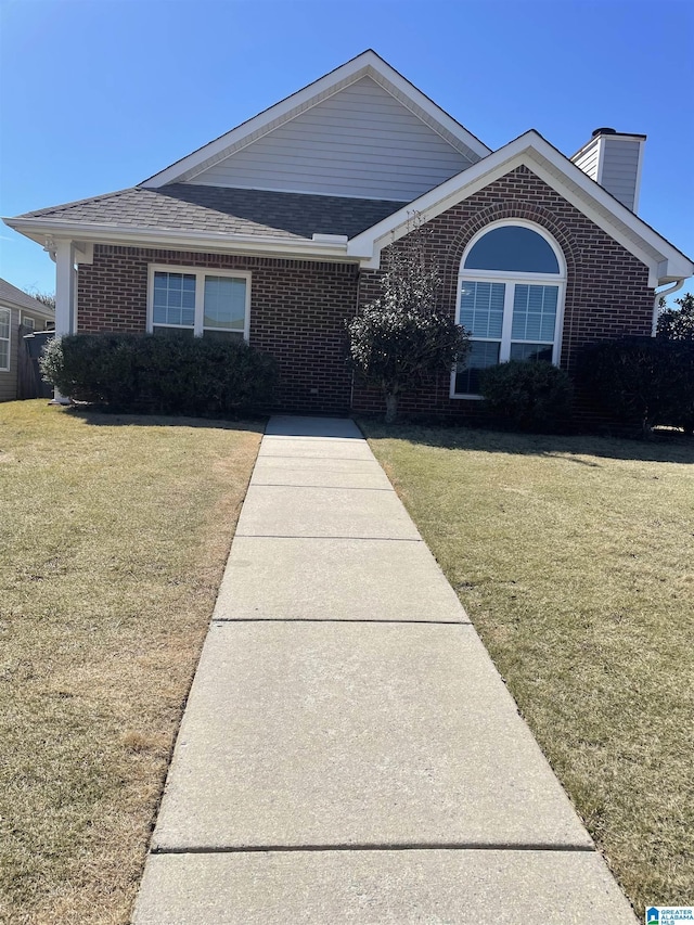 view of front of house with brick siding, a chimney, a front yard, and roof with shingles