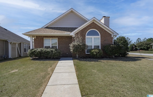 view of front of home featuring brick siding, a chimney, a front yard, and a shingled roof