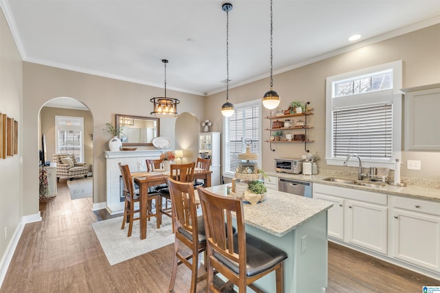 kitchen with arched walkways, wood finished floors, stainless steel dishwasher, and a sink