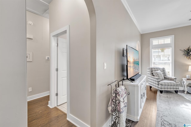 corridor featuring baseboards, wood finished floors, arched walkways, and ornamental molding