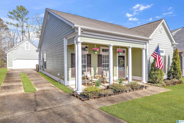 view of front facade featuring an outbuilding, driveway, covered porch, a shingled roof, and a front lawn