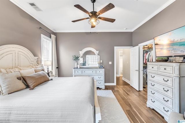 bedroom featuring visible vents, a walk in closet, crown molding, ceiling fan, and wood finished floors